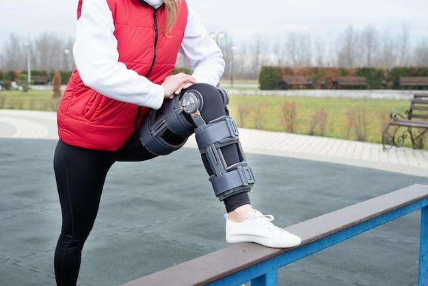 Photo woman wearing knee brace or orthosis after leg surgery working out in the park