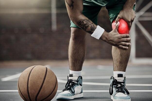 Photo sports injury in basketball and knee pain or athlete man while on an outdoors court holding his hurt leg during training or exercise for hobby closeup of male hands on glowing red body part
